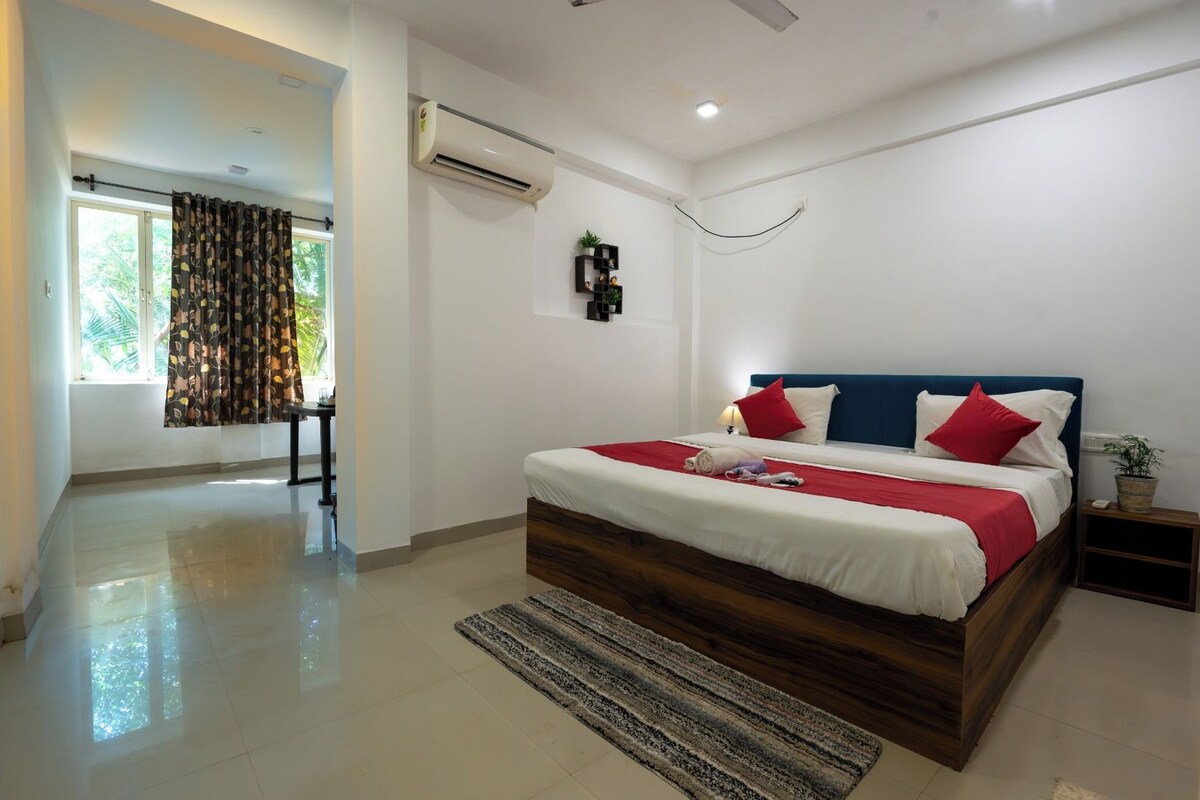 Um quarto moderno com uma cama grande, uma mesa de cabeceira, um criado-mudo, um aparelho de ar condicionado e uma janela com cortinas.