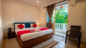 Une chambre avec un lit en bois, une literie rouge et blanche, une petite table de chevet avec une plante, et une vue sur la verdure par la porte d'un balcon.