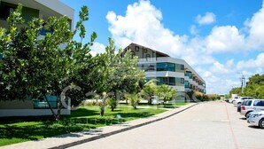 Un edificio moderno con fachada curva, un estacionamiento con coches y un césped bien cuidado con árboles.