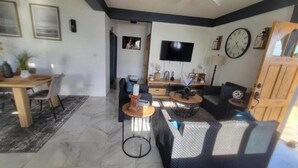 A modern living room with a sofa, coffee table, and TV. There is a dining area with a table and chairs. - Visconti Guest House (Cottage)
