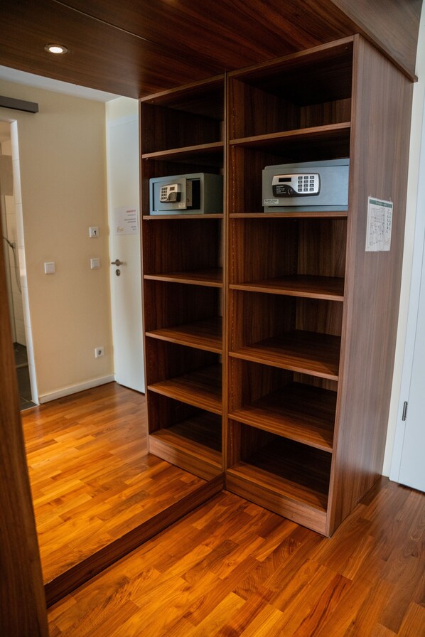 A wooden shelving unit with electronic devices on top, a wooden floor, and a white door with a sign. - Hotel am Schlosspark (Worms)
