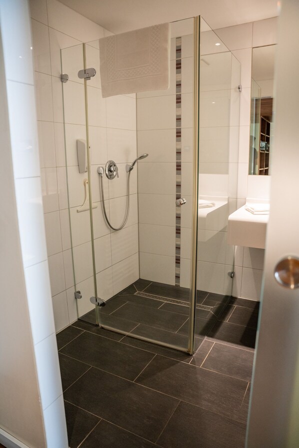 A modern bathroom with a glass-enclosed shower, a white sink, and dark tiled flooring.