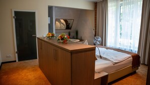 Une chambre d’hôtel avec un lit, une commode en bois, un miroir, un lavabo et une fenêtre avec des rideaux.