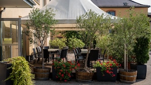 Un espace extérieur aménagé avec des tables et des chaises, entouré de plantes en pot et d’arbres.