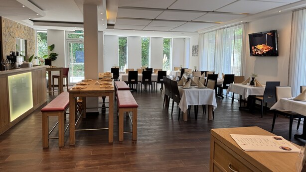 Un restaurant spacieux avec des tables et des chaises en bois, un coin bar et de grandes fenêtres donnant sur un paysage verdoyant.