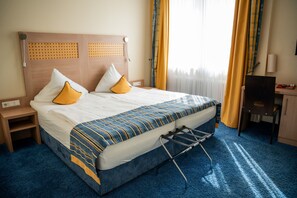 Quarto de hotel com uma cama, uma escrivaninha e uma cadeira.
