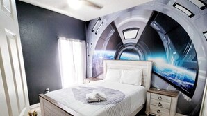 Un dormitorio con cama, mesita de noche, ventilador de techo y un mural en la pared.