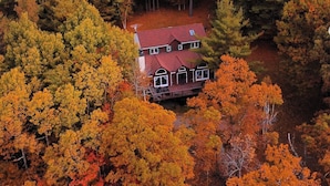 An aerial view of a house surrounded by dense forest with autumn foliage.