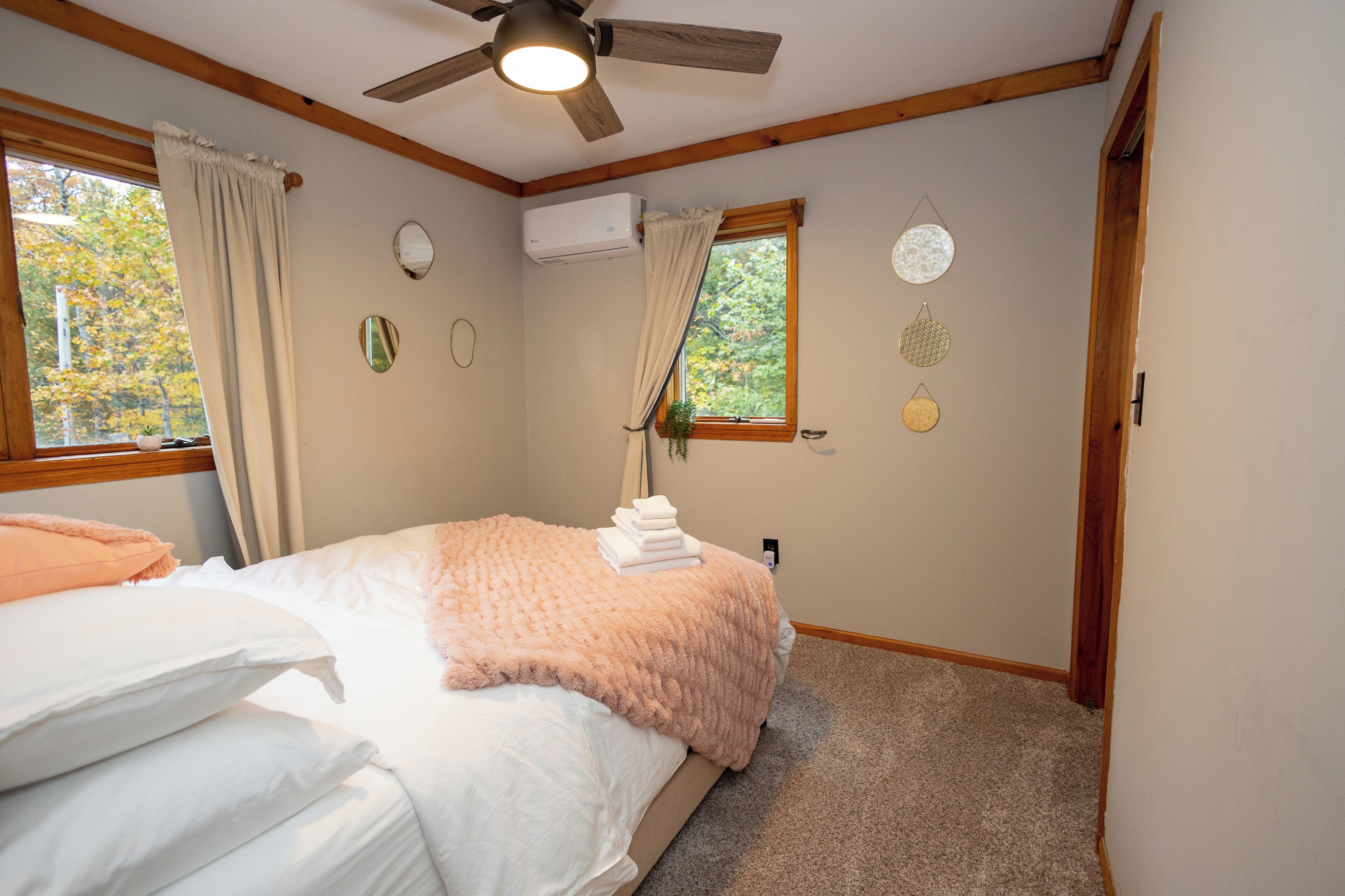A bedroom with a bed, a ceiling fan, a window with curtains, an air conditioning unit, and wall decorations.