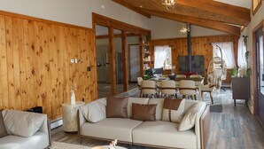 A cozy living room with a wooden wall, a sofa, a coffee table, and a dining area with chairs and a table.