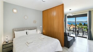 A modern bedroom with a large bed, bedside tables, a nightstand, a desk, and a view of the sea.