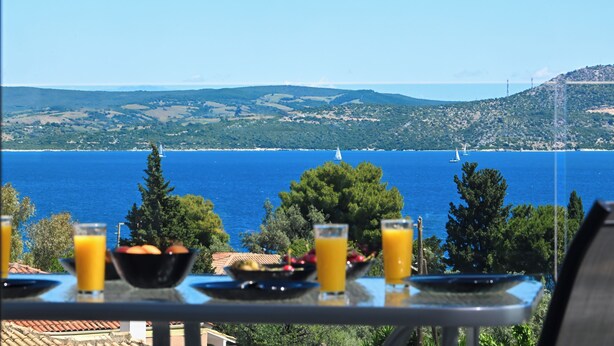 A table with breakfast items and a scenic view of the sea and hills.
