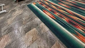 Un dormitorio con dos camas, una pared decorativa de piedra, una alfombra grande y colorida, y una silla pequeña.