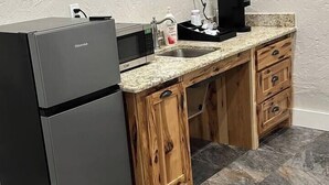 Una cocina compacta con refrigerador negro, armarios de madera, encimera de granito y cafetera.