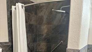 Un área de ducha con puerta de vidrio curva, barandilla y suelo de baldosas.