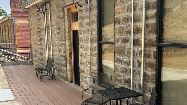 Un edificio de piedra con terraza de madera, asientos exteriores y ventanas amplias.