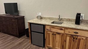 A compact kitchen with wooden cabinets, a granite countertop, a stainless steel sink, and a built-in dishwasher. - The Cross Bell Downtown 202 (Pawhuska)