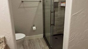 A small bathroom with a toilet, a glass shower enclosure, and a marble countertop. - The Cross Bell Downtown 202 (Pawhuska)