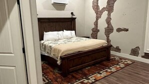 A bedroom with a wooden bed, a patterned rug, a ceiling fan, and a wall with a brick-like design. - The Cross Bell Downtown 202 (Pawhuska)