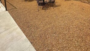 An outdoor seating area with tables and chairs, a stone retaining wall, and a building in the background. - The Cross Bell Downtown 202 (Pawhuska)