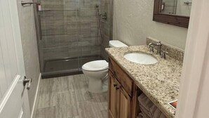 A bathroom with a glass-enclosed shower, a toilet, and a sink with a granite countertop. - The Cross Bell Downtown 201 (Pawhuska)