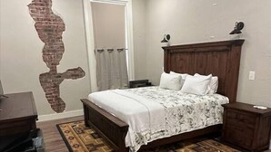 A bedroom with a wooden bed, a nightstand, a dresser, a ceiling fan, and a patterned rug. - The Cross Bell Downtown 201 (Pawhuska)