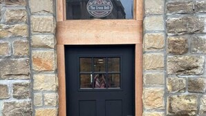 A black door with a stone facade, a small window above it, and a logo on the window. - The Cross Bell Downtown 201 (Pawhuska)