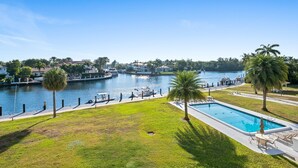 A swimming pool with a view of a lake, surrounded by grass and palm trees.