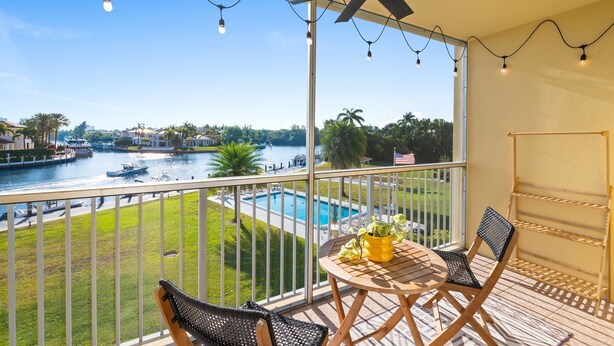 A balcony with a view of a river, a pool, and a chair with a plant.