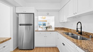 A modern kitchen with white cabinets, a stainless steel refrigerator, granite countertops, and a double sink.