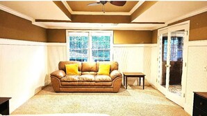 A living room with a brown leather sofa, two yellow cushions, a small table, and a ceiling fan. - Get cozy in this 2-bedroom garden apartment in peaceful Alpharetta. (Alpharetta)