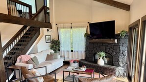 A living room with a stone fireplace, a sofa, two leather chairs, a coffee table, and a TV. - Magnificent, newly remodeled Snowmass Condo (Snowmass Village)