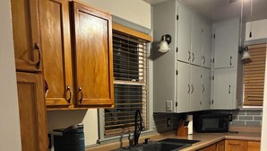 Una cocina con armarios de madera, lavavajillas, microondas y ventana con persianas.