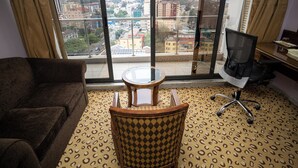 Une pièce comprenant un canapé, une petite table ronde, un tapis à motifs et une vue sur le paysage urbain, visible à travers de grandes fenêtres.