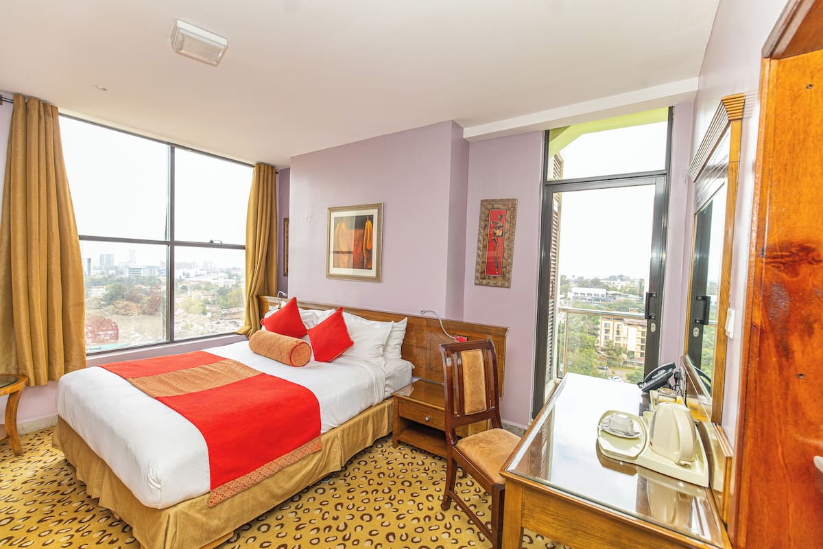 Une chambre d’hôtel avec un grand lit, un bureau avec une chaise et une vue sur la ville par les fenêtres.