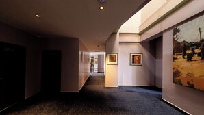 Un couloir doté d’un sol recouvert de moquette, avec des œuvres d’art encadrées accrochées aux murs et des portes sur le côté gauche.
