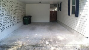 Un garage fermé avec un sol en béton, une clôture blanche en treillis sur la gauche et une clôture en bois à l’arrière-plan.