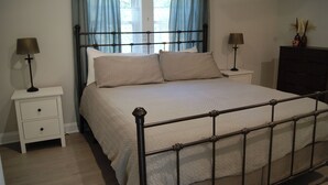 Une chambre à coucher avec un lit en métal, deux tables de chevet avec des lampes, une commode et une fenêtre avec des rideaux.
