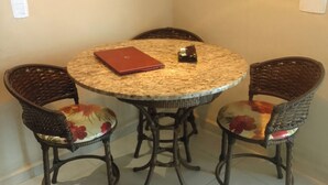 Una mesa redonda con una silla de diseño trenzado, una computadora portátil y un objeto pequeño sobre la mesa.