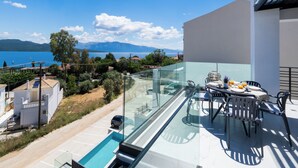 En moderne balkon med gelænder af glas, der giver udsigt over en smuk sø og bjerglandskab.