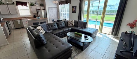 A modern living room with a sectional sofa, a coffee table, and a view of a swimming pool through large sliding glass doors.