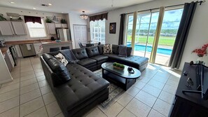 A modern living room with a sectional sofa, a coffee table, and a view of a swimming pool through large sliding glass doors.
