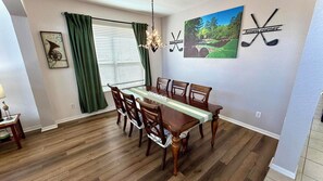 Un coin repas avec une table et des chaises en bois, un lustre et une décoration murale sur le thème du golf.