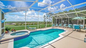 A covered outdoor swimming pool with a view of a golf course, surrounded by lounge chairs and umbrellas.