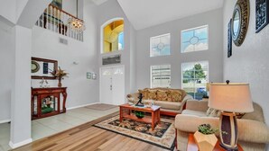 A spacious living room with a high ceiling, a wooden coffee table, a sofa, and a lamp.