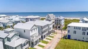 A coastal residential area with multiple two-story houses, a clear view of the beach, and a stop sign in the foreground. - Beachtown - STEPS FROM BEACH & POOL - Breathtaking 5-bedroom house w/Elevator! (Galveston)