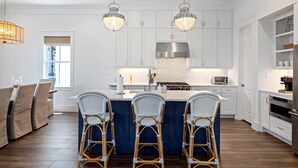 A modern kitchen with white cabinets, a central island with bar stools, and stainless steel appliances. - Beachtown - STEPS FROM BEACH & POOL - Breathtaking 5-bedroom house w/Elevator! (Galveston)