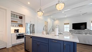 A modern kitchen with a central island, built-in appliances, and a large flat-screen TV. - Beachtown - STEPS FROM BEACH & POOL - Breathtaking 5-bedroom house w/Elevator! (Galveston)