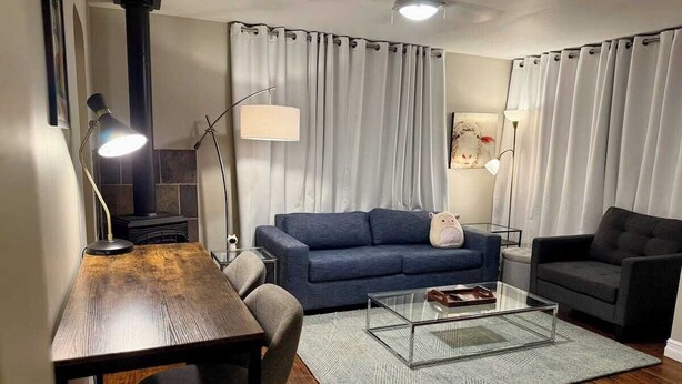 En moderne stue med en blå sofa, et glasbord, et træspisebord og en sort lænestol.
