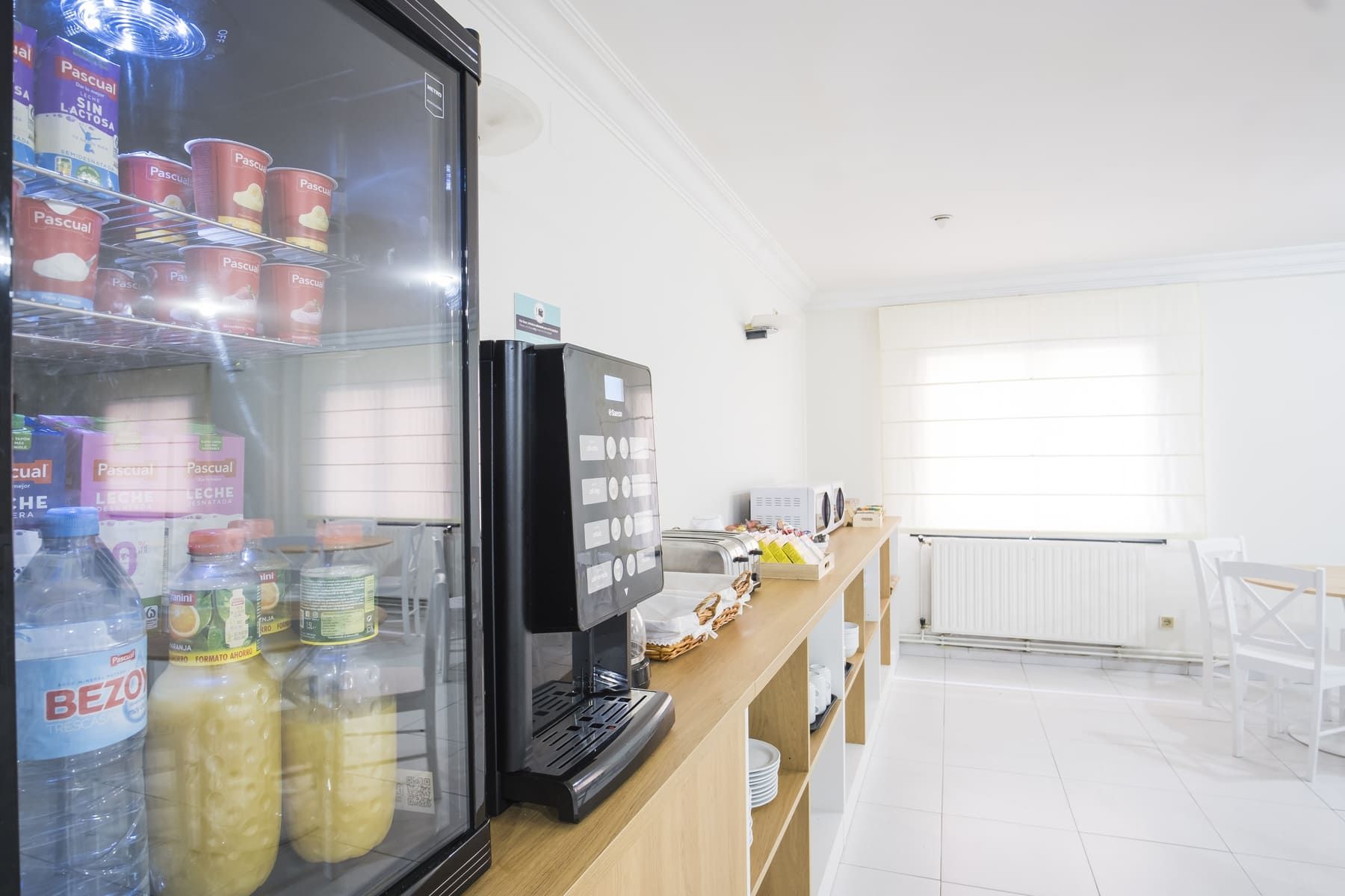 Una kitchenette con un refrigerador lleno de bebidas, un tostador y una cafetera.